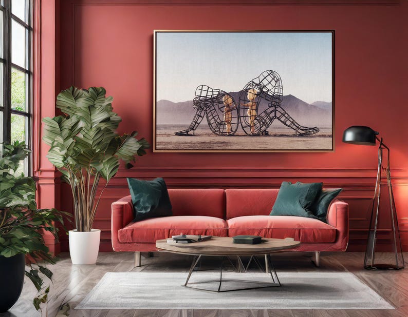 May include: A living room with a red sofa, teal pillows, and a wooden coffee table. A large framed artwork depicts wireframe figures on a desert landscape. A tall plant in a white pot and a black floor lamp complete the decor.