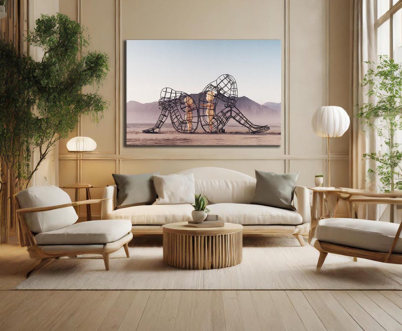May include: A large framed artwork depicts two wireframe human figures in a seated embrace against a desert landscape. The room features a cream-colored sofa, wooden furniture, and a neutral color palette.