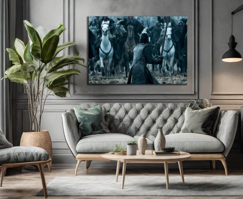 May include: A large canvas print depicting a battle scene with riders on horseback. The artwork is mounted above a gray tufted sofa with wooden legs. A large potted plant and decorative items complete the room's decor.