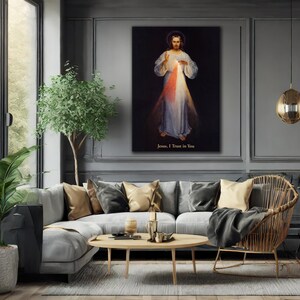 May include: A framed canvas print of Jesus with a halo, wearing a white robe, with red and white light emanating from his chest. The text "Jesus, I Trust in You" is at the bottom. The print hangs above a gray sofa in a living room.