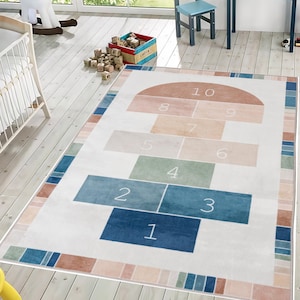 Può includere: Un tappeto rettangolare a campana con sfondo bianco e design colorato a campana. La griglia della campana presenta quadrati numerati in tonalità di blu, verde e pesca. Il tappeto ha un bordo con strisce blu, verdi e pesca.