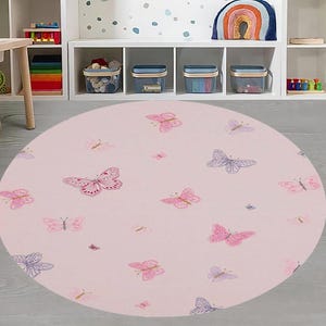 May include: A round, light pink rug featuring a pattern of various pink and purple butterflies. The butterflies are in different sizes and styles, scattered across the rug. This rug is suitable for a child's room or play area.