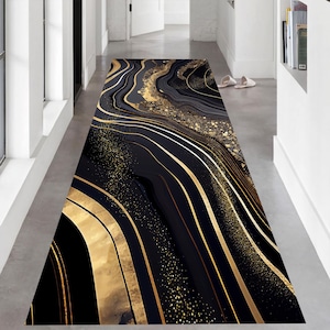 Può includere: Un lungo tappeto rettangolare con un design astratto nero e oro. Il tappeto presenta motivi fluidi a forma di onda in nero, accentuati da linee e macchie dorate. Il design crea un'estetica lussuosa e moderna, adatta per un corridoio o un ingresso.