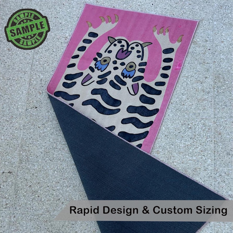 Puede incluir: Alfombra rosa con un dise&ntilde;o de tigre de dibujos animados en crema y azul marino. La alfombra tiene un reverso azul oscuro y el texto "Rapid Design & Custom Sizing". Un sello verde "SAMPLE" est&aacute; en la esquina superior izquierda.