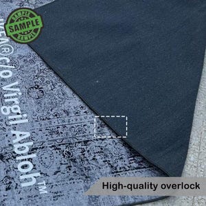 Puede incluir: Una secci&oacute;n de una alfombra gris y negra estampada con un borde de sobrehilado gris oscuro. La alfombra tiene un aspecto envejecido y vintage. El texto "SAMPLE" est&aacute; en un c&iacute;rculo verde. El texto "High-quality overlock" es visible.