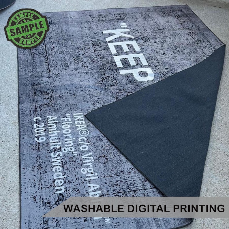 Puede incluir: Una alfombra rectangular gris con un patr&oacute;n floral desgastado y la palabra "KEEP" en letras blancas grandes. La alfombra tiene un reverso gris oscuro e incluye el texto "IKEA c/o Virgil Ab" y "Washable Digital Printing."