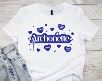Op de afbeelding: Wit T-shirt met een blauw ontwerp met het woord "Archonette" en hartvormige afbeeldingen. Het ontwerp bevat de woorden "scholarship", "service" en "sisterly love".
