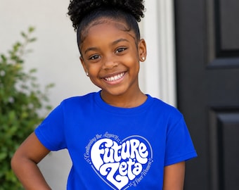 Op de afbeelding: Een koningsblauw T-shirt met korte mouwen en een witte hartvormige afbeelding. Binnenin het hart staat de tekst Future Zeta in een vet retro lettertype, met de zinnen Continuing the Legacy en of Finer Women langs de randen geschreven.