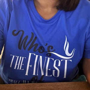 May include: A bright blue short-sleeved t-shirt featuring the text "Who's THE FINEST" printed on the front. The word "Who's" is in black script, while "THE FINEST" is in large white capital letters with a white graphic swirl design.