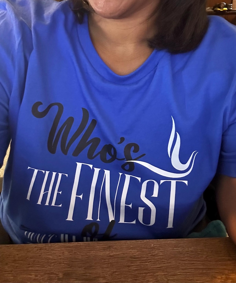 May include: A bright blue short-sleeved t-shirt featuring the text "Who's THE FINEST" printed on the front. The word "Who's" is in black script, while "THE FINEST" is in large white capital letters with a white graphic swirl design.