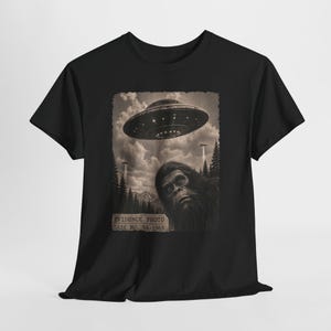 Könnte beinhalten: Schwarzes T-Shirt mit einem Sepia-Ton-Grafik eines UFOs über einem Wald und einem Bigfoot. Der Text "EVIDENCE PHOTO CASE NO. 9A-1969" ist ebenfalls enthalten.