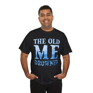 Puede incluir: Camiseta negra con el texto "THE OLD ME DROWNED" en azul y blanco. La palabra "ME" está diseñada con un gráfico de agua y cielo. La camiseta es de cuello redondo.