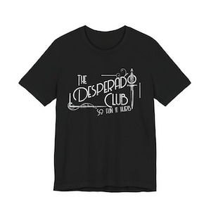 May include: Black t-shirt featuring the white text "The Desperado Club" and a sword graphic. The phrase "So fun it hurts" is printed below the club name. The shirt has short sleeves and a crew neck.