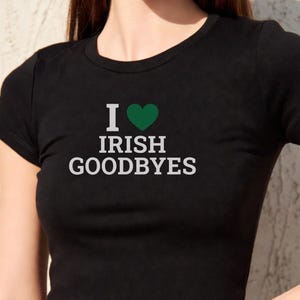 Pode incluir: Top preto curto com o texto "I ♥ IRISH GOODBYES" em branco, com um coração verde. A blusa tem gola redonda e mangas curtas. A camisa é feita de um material macio.