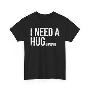 Puede incluir: Una camiseta negra de manga corta con texto blanco de estilo desgastado en el pecho que dice I NEED A HUGE GARAGE. Las letras están dispuestas en tres líneas, con la palabra HUGE en un tamaño de fuente mayor que el resto del texto.