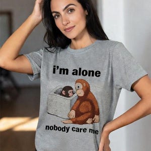 May include: Gray t-shirt with the text "I'm alone nobody care me" and a cartoon illustration of two orangutans. One orangutan is sitting outside a box, and the other is inside.