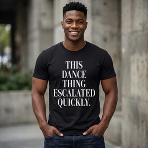 Puede incluir: Camiseta negra con el texto blanco "THIS DANCE THING ESCALATED QUICKLY". La camiseta es de cuello redondo y se está usando.