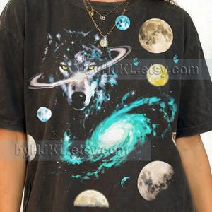 May include: A white ceramic mug with a black handle and the text "But First, Coffee" in a bold, black font. The mug is set against a blurred background, suggesting a cozy setting.