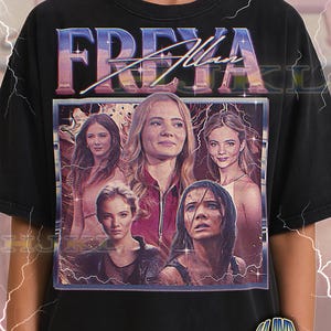 Może przedstawiać: Czarna koszulka unisex dla dorosłych z grafiką w stylu retro. Grafika przedstawia słowo "FREYA" i kolaż twarzy kobiet. Na koszulce widoczny jest również napis "ADULT Unisex Shirt : BLACK".