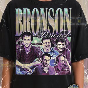 May include: Black adult unisex t-shirt featuring a graphic of the word "BRONSON" in a retro font, with the name "Pinchot" below. The shirt displays a collage of five men. The text "ADULT Unisex Shirt : BLACK" is at the bottom.