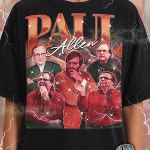 May include: Black adult unisex t-shirt featuring a vintage-style graphic of a man in various poses. The graphic includes the name "Paul Allen" in a retro font. The shirt has the text "ADULT Unisex Shirt : BLACK" at the bottom.