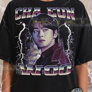 Może przedstawiać: Czarna koszulka unisex dla dorosłych z retro wzorem z napisem "CHA EUN WOO" i portretem. Projekt zawiera błyskawice i estetykę vintage. Koszulka ma również napis "ADULT Unisex Shirt : BLACK".