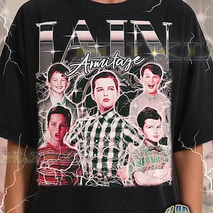 May include: Black adult unisex t-shirt featuring a graphic of Iain Armitage with multiple images of him. The word "IAIN" is at the top, and "Armitage" is below. The shirt has a vintage look with lightning bolt effects.