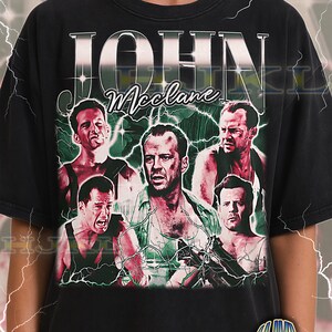 Puede incluir: Camiseta negra unisex para adultos con un diseño gráfico de estilo vintage de John McClane de la película Die Hard. El diseño incluye múltiples imágenes del personaje con el nombre "JOHN McClane" en negrita. La camiseta también tiene el texto "ADULT Unisex Shirt : BLACK".