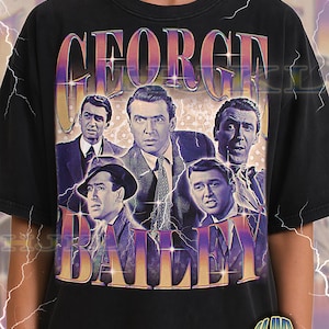 May include: Black adult unisex t-shirt featuring a vintage design with the text "GEORGE BAILEY" in a purple and orange gradient. The graphic includes images of actors. The shirt has a distressed look.