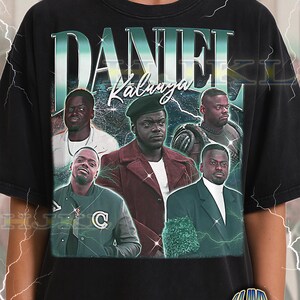 Puede incluir: Camiseta negra unisex para adultos con un diseño gráfico que presenta el nombre "DANIEL Kaluuya" en texto grande y estilizado. El diseño incluye múltiples imágenes de un hombre. La camiseta tiene un aspecto vintage y desgastado.