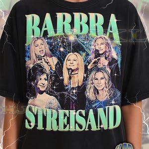 May include: Black adult unisex t-shirt featuring a graphic of Barbra Streisand with the text "BARBRA STREISAND" in a retro style. The design includes multiple images of the singer with a lightning bolt background. The shirt also has the text "ADULT Unisex Shirt : BLACK".