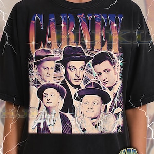 May include: Black adult unisex t-shirt with a retro graphic of a group of men and the word "CARNEY" in a colourful font. The word "Art" is also visible. The shirt has a vintage, worn appearance.
