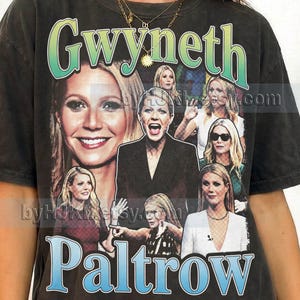 Peut inclure: Un t-shirt gris anthracite à manches courtes présentant un collage de diverses photographies de Gwyneth Paltrow. Le nom Gwyneth est imprimé dans une police à dégradé vert en haut, et Paltrow est imprimé dans une police à dégradé bleu en bas.