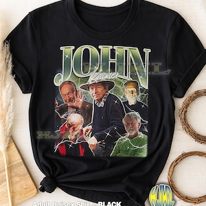 Könnte beinhalten: Schwarzes Unisex-T-Shirt für Erwachsene mit einem Vintage-Grafik von John Kramer und anderen Charakteren. Das Design enthält den Namen "JOHN KRAMER" in einer grünen, verwitterten Schriftart. Das Shirt besteht aus weichem Material und hat einen klassischen Rundhalsausschnitt.
