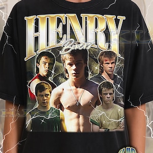 Puede incluir: Camiseta negra unisex para adultos con un gráfico dorado del nombre "HENRY Bowers" sobre un collage de jóvenes. La camiseta tiene un aspecto vintage y el texto "ADULT Unisex Shirt : BLACK" está impreso en la parte inferior.