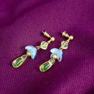 Pode incluir: Um par de brincos pendentes com pinos de metal dourado, pequenas contas quadradas verde-limão translúcidas, contas azul-claras em forma de flor, pequenas contas esféricas douradas e pingentes de vidro em forma de gota na cor verde-limão.
