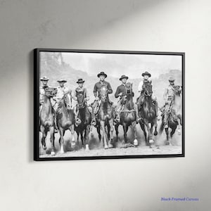 以下が含まれることがあります： 白黒の額入りキャンバスプリント。カウボーイのグループが馬に乗っています。カウボーイは帽子をかぶり、馬に乗って一列に並び、埃を立てています。「Black Framed Canvas」の文字が右下にあります。