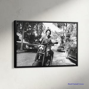 May include: Monochrome framed canvas print showing a person on a motorcycle. The motorcycle has a prominent headlight and is on a road with cars and trees. The text "Black Framed Canvas" is in the bottom right corner of the image.