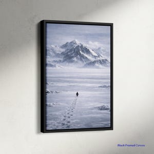 May include: A framed canvas print depicts a solitary figure walking across a snowy landscape toward a mountain range. The artwork is in shades of gray and white, with a black frame. The text "Black Framed Canvas" is visible in the lower right corner.
