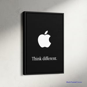 Puede incluir: Lienzo enmarcado en negro con el logotipo de una manzana blanca y la frase "Think different". La obra de arte tiene un diseño minimalista con fondo negro y texto blanco. El lienzo es rectangular y está montado en un marco negro.