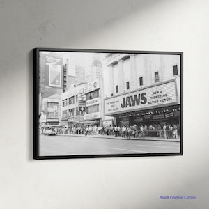Könnte beinhalten: Schwarz-Weiß-Leinwanddruck mit Rahmen eines Vintage-Kinoplakats mit der Aufschrift "JAWS". Das Bild zeigt eine Menschenmenge vor dem Kino, mit anderen Gebäuden und Werbung im Hintergrund.
