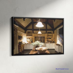 May include: A framed canvas print of a kitchen interior. The kitchen features white cabinets, a brick fireplace, and a wooden table. Two pendant lights hang from the ceiling. A bowl of bread and flowers sits on the table.