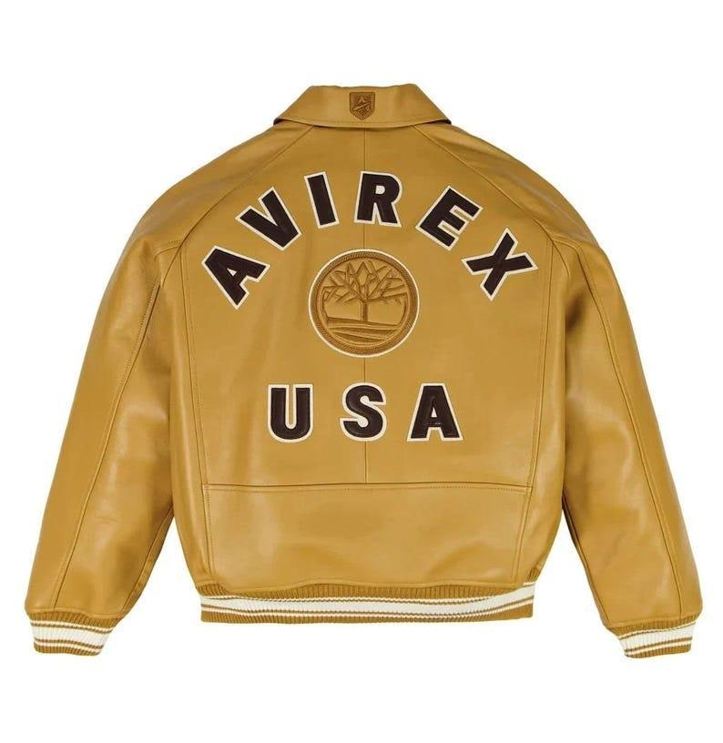 Puede incluir: Chaqueta de cuero amarillo mostaza con el texto "AVIREX USA" en la espalda. La chaqueta tiene cuello, pu&ntilde;os y dobladillo acanalados con rayas blancas. Un logotipo de &aacute;rbol est&aacute; centrado entre las palabras "AVIREX" y "USA".