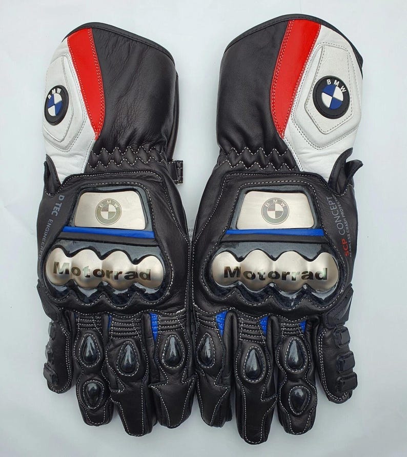 K&ouml;nnte beinhalten: Paar schwarze Motorradhandschuhe aus Leder mit wei&szlig;en, roten und blauen Akzenten. Mit BMW-Logo und dem Wort "Motorrad" in Silber. Inklusive Kn&ouml;chel- und Handgelenkschutz.