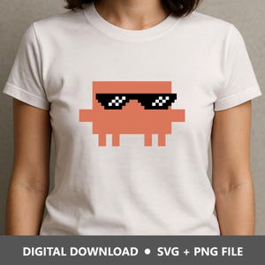 May include: A white short-sleeved t-shirt featuring a central pixelated orange character graphic wearing black pixelated sunglasses. The bottom of the image includes the text: DIGITAL DOWNLOAD • SVG + PNG FILE.