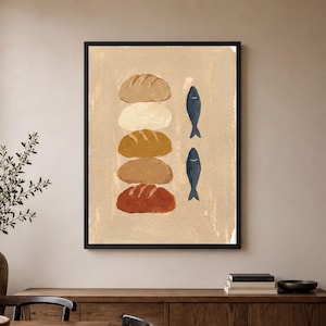 May include: A framed wall art print featuring a vertical stack of five stylized loaves of bread in shades of tan, cream, gold, brown, and terracotta, positioned next to two dark blue fish illustrations on a textured light beige background.