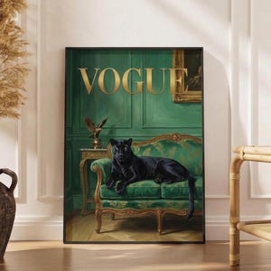 A framed poster of a black panther sitting on a green couch, with the word "Vogue" written on the poster. The poster is displayed on a wall, and there is a vase and a wooden table nearby.