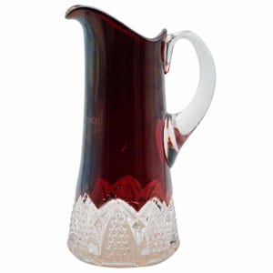 May include: A ruby red glass pitcher with a clear handle. The top portion of the pitcher is a deep red, transitioning to a clear, patterned base. The handle is clear glass. The pitcher has a spout for easy pouring.