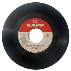 May include: A black vinyl record with a red and white label. The label reads "KAPP" and features the song title "UNTIL MY HEART FOUND YOU" by Mimi Roman. The record is marked "NOT FOR SALE".