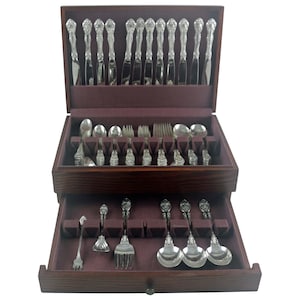 May include: A wooden silverware chest with multiple drawers, lined with a deep purple fabric. The chest is filled with ornate silver cutlery, including knives, forks, spoons, and serving pieces. The silverware has decorative handles.